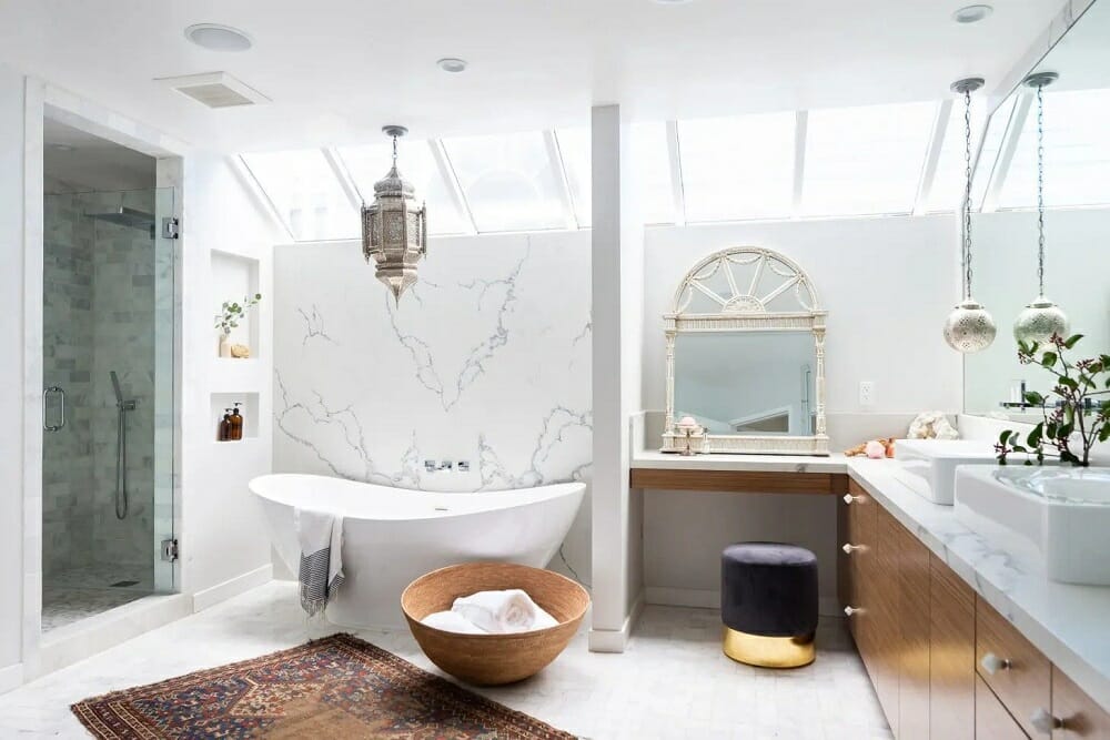 Freestanding bathtub with a chandelier, rug and ornate mirror in a large bathroom on trend for master bathroom trends