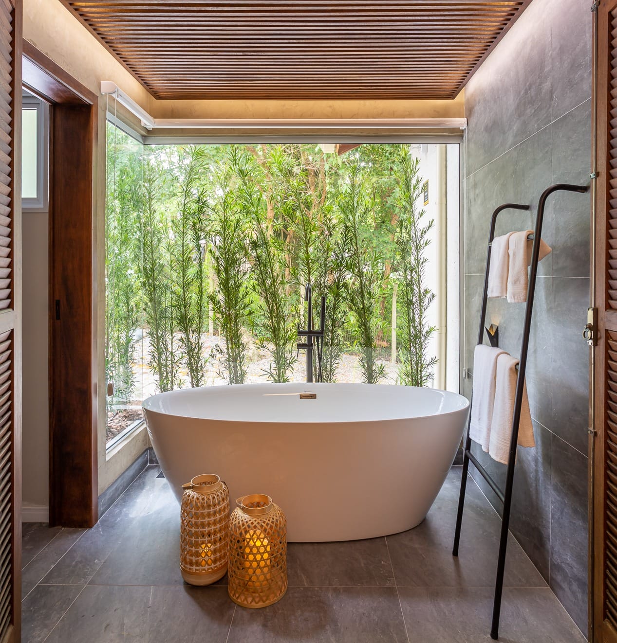 Asian Zen bathroom with a freestanding oval bathtub, bamboo garden view, gray stone tile, slatted wood ceiling and woven lanterns