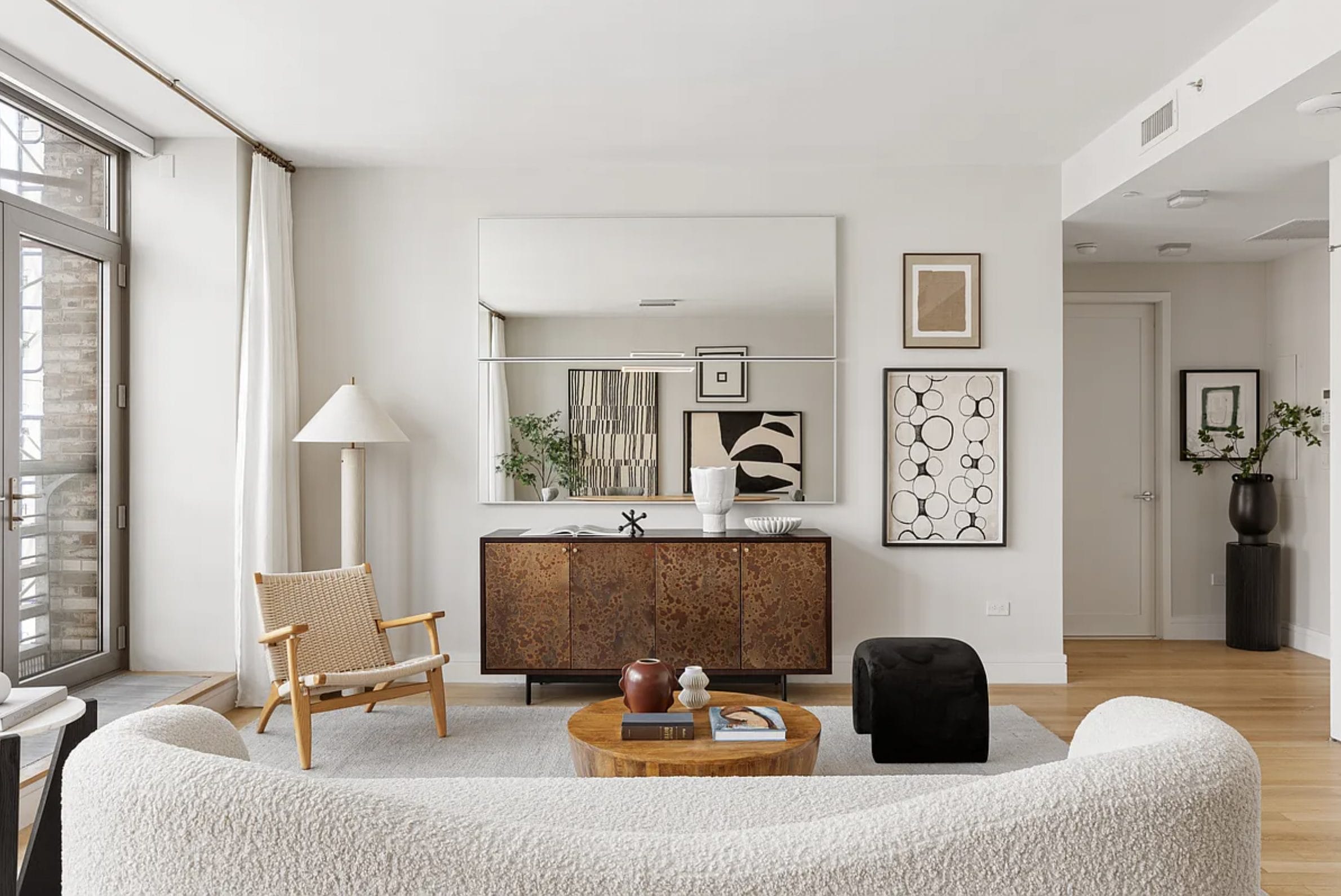 Scandinavian-inspired living room with a curved white sofa, woven wood chair, burl wood cabinet and round wood coffee table