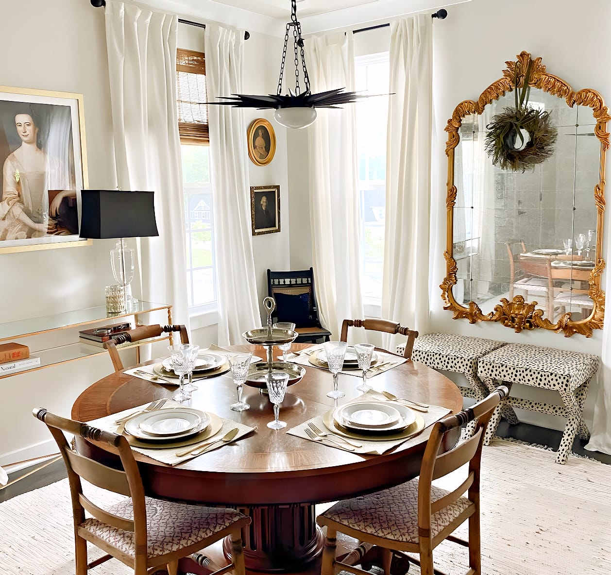 Traditional dining room with a round wood table, antique chairs, formal place settings, portraits and an ornate gold mirror
