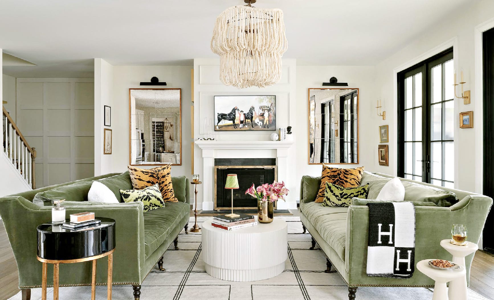 Transitional living room with facing green velvet sofas, a white fireplace, framed mirrors and a beaded chandelier